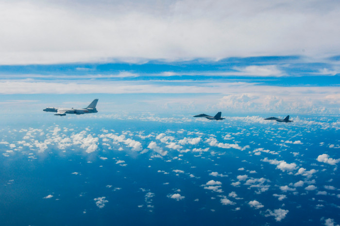 Two Chinese fighter jets and a larger plane fly over the Taiwan Strait with blue sky and white clouds in the background