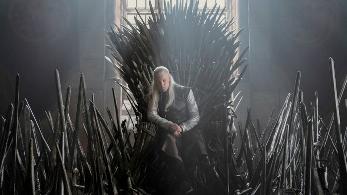 A sinister figure with long white-blond hair sits on what looks like a throne made of spikes or spearheads 