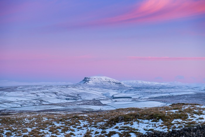 Pen-y-ghent, the lowest of the Yorkshire Three Peaks, seen in the distance on a snowy day, beneath a violet sky