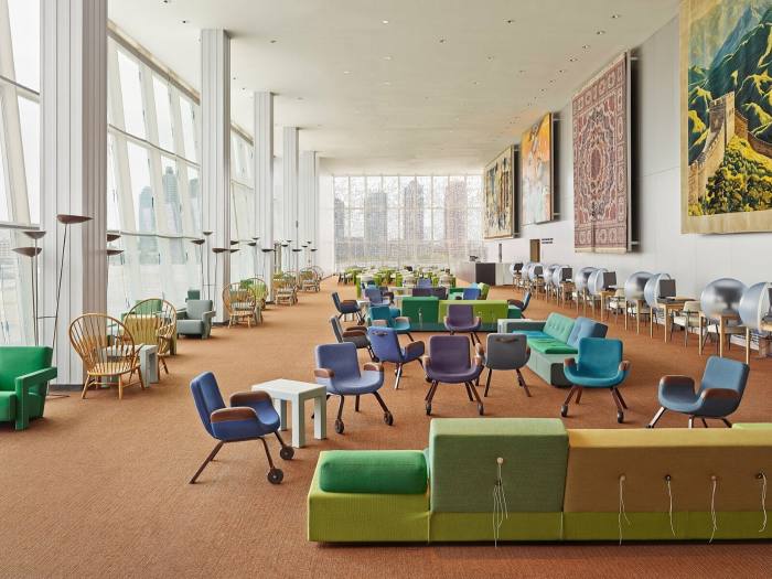 A large room, bright with natural light, has seats and sofas in shades of green and blue