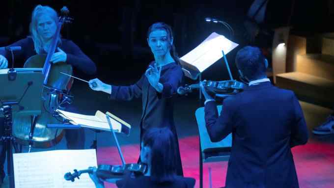 A woman conducts orchestral players