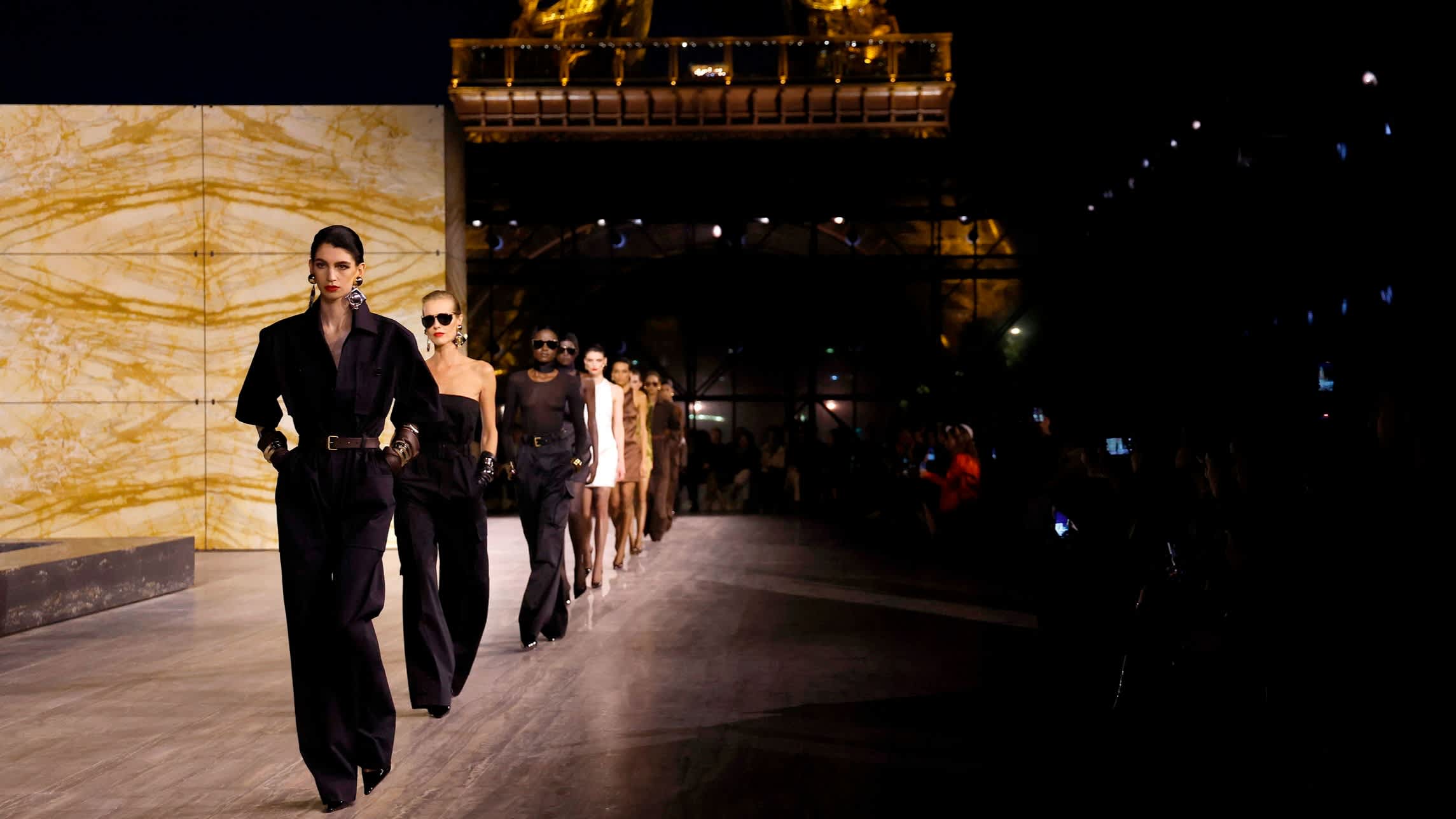 A row of catwalk models walk under the Eiffel Tower during the Saint Laurent spring/summer 24 show