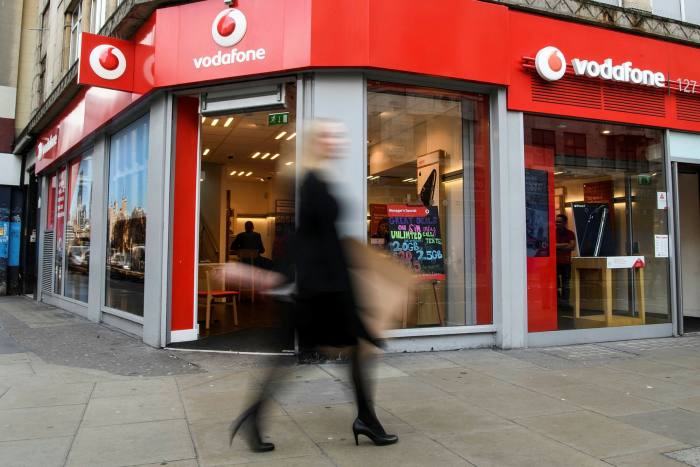 People walk past a branch of the telecommunications company Vodafone in London