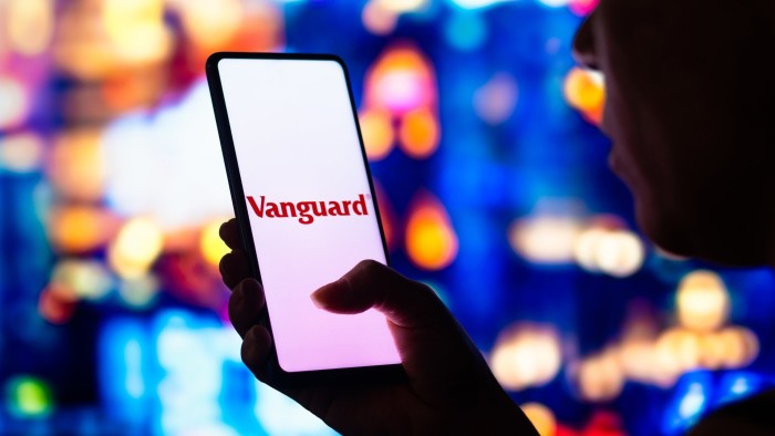 A woman holds a smartphone with the Vanguard Group logo displayed on the screen