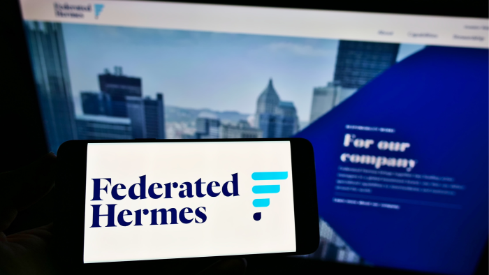 The Federated Hermes logo on a smartphone in front of its website on a computer screen 