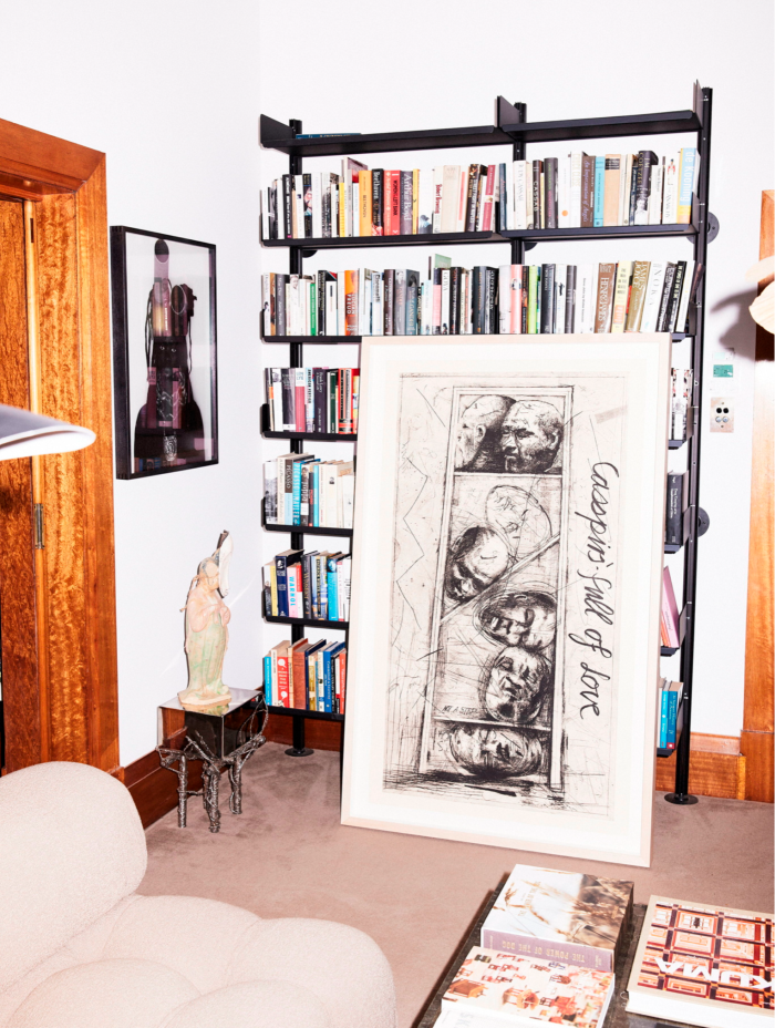 A large black line drawing in a frame is propped up against a bookshelf