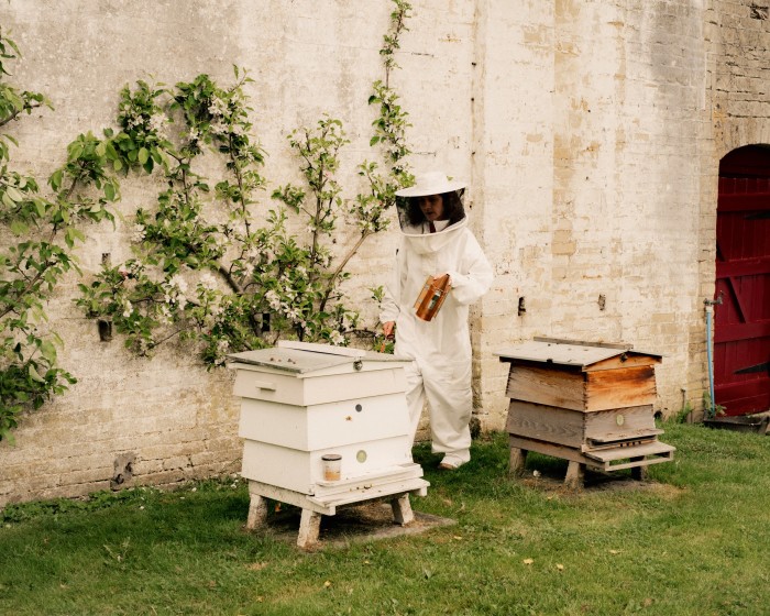 Nicola in her bee suit next to hives in the walled garden
