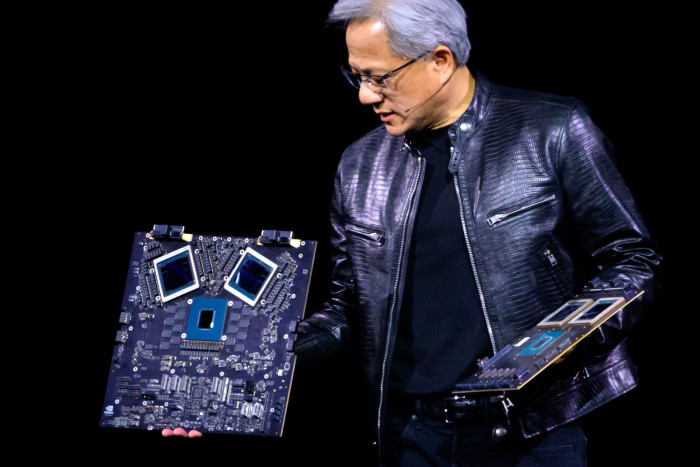 A man in a black leather jacket holds up a circuit board