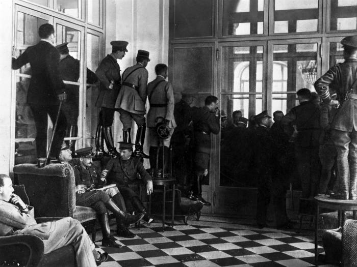 Allied officers stand on chairs to get a glimpse into the Hall of Mirrors where the Treaty of Versailles was being signed in 1919