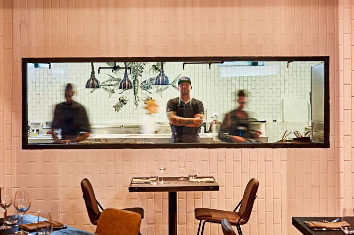 Jeremy Ford in his kitchen at Stubborn Seed, seen through the window of a large rectangular hole in the dining space’s pink-brick wall