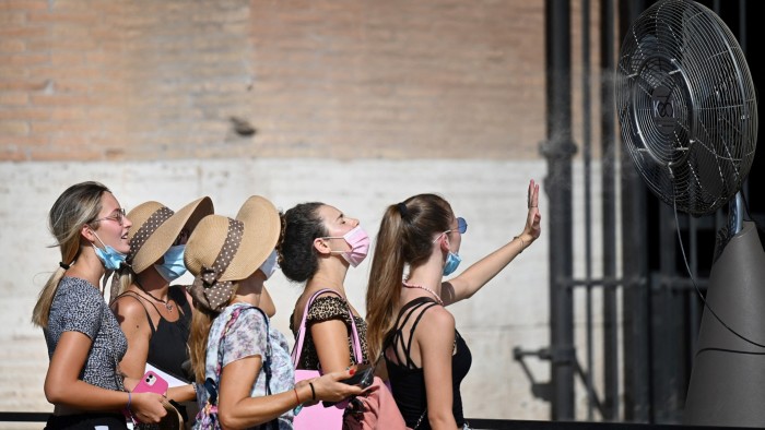 A line of five women stand in front of a cooling fan in Rome during the August 2022 heatwave