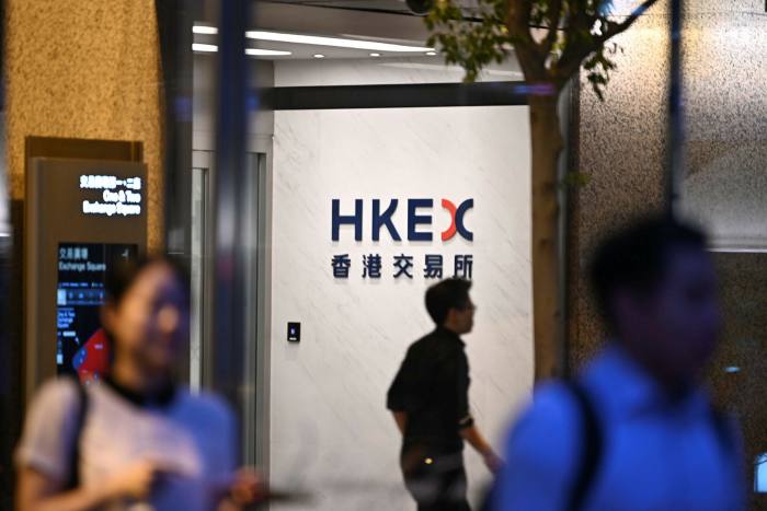 People are seen walking pass a logo of the Hong Kong Stock Exchange in Hong Kong