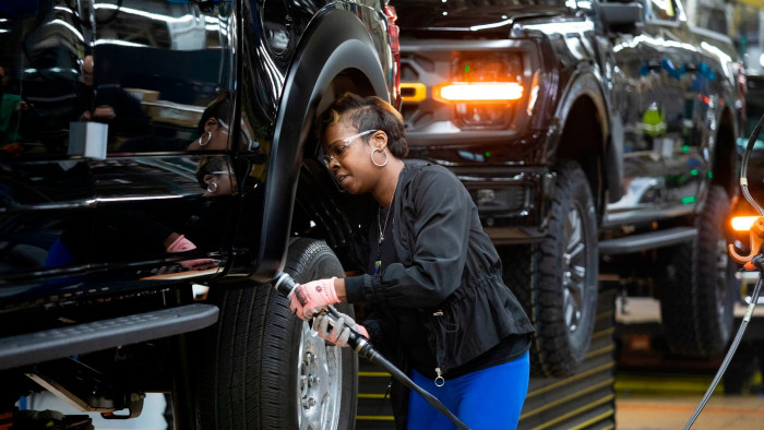 A man inspects a Ford pick-up truck as it moves along an assembly line