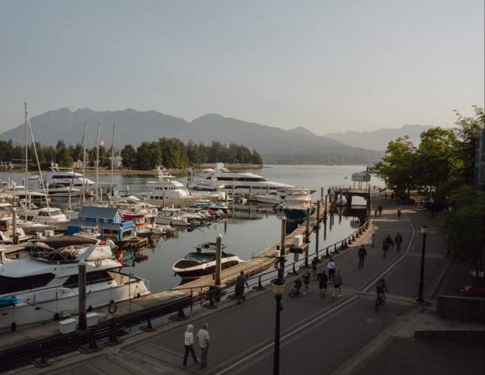 Pedestrians walking along Coal Harbour Seawall, with boats on the harbour to its left and 