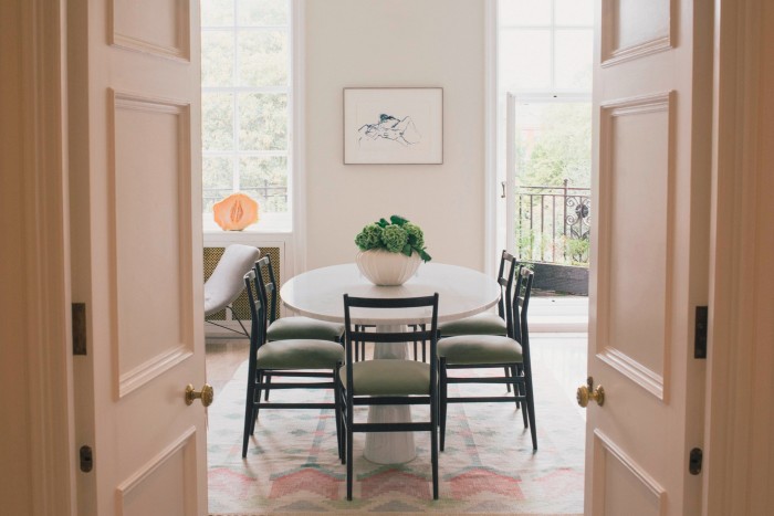 Double doors open into an airy, sunlit dining room with white walls and matching black chairs