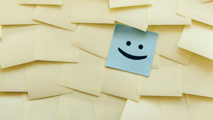 Many yellow Post-it notes on a board, with a special blue one with a happy face drawn on it