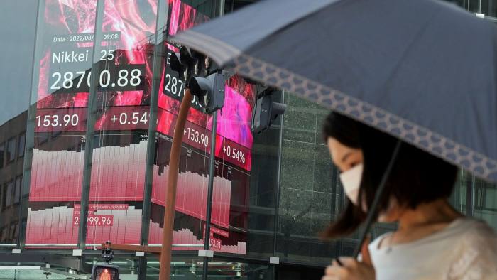 A person wearing a protective mask walks past an electronic stock prices board in Tokyo