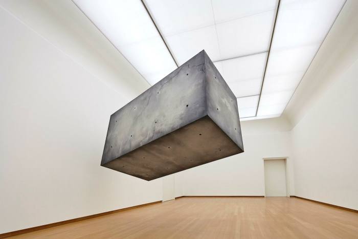 A large dirty-looking concrete block floats in the middle of a white room
