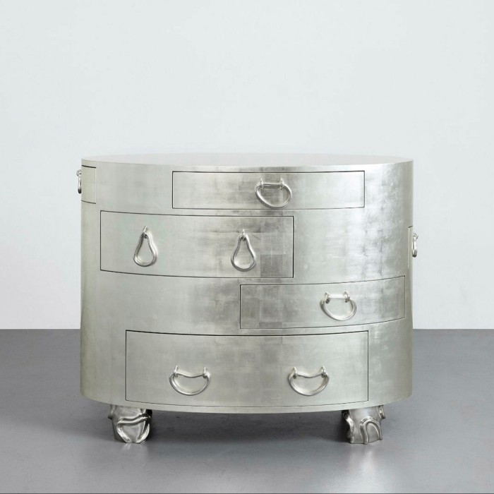 A round, silver-looking chest of drawers features multiple handles