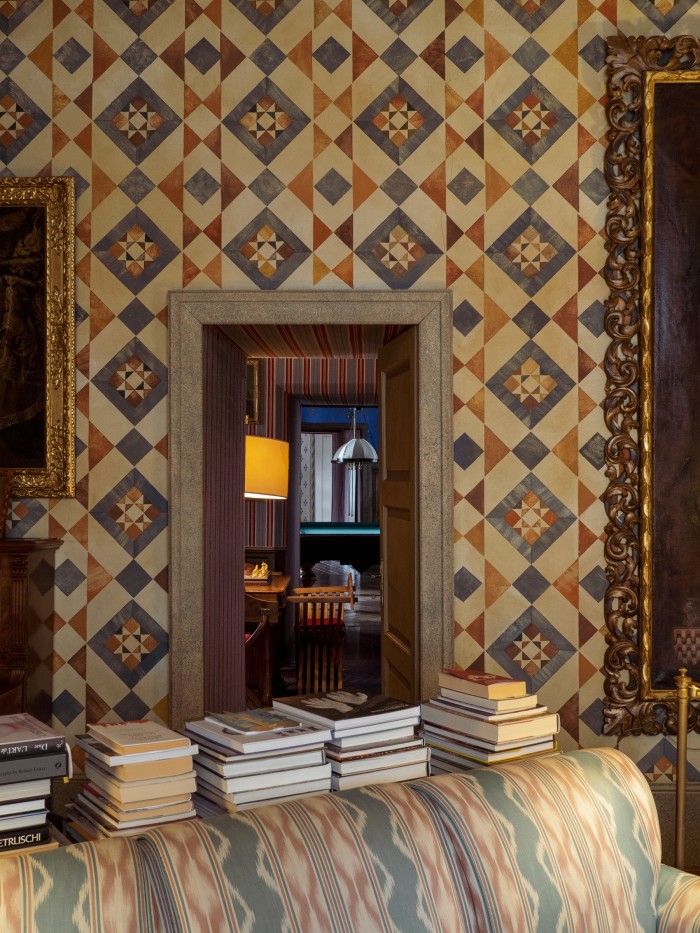 Piles of books in the small living room, with a view through the contrasting wallpapers to the Billiard room