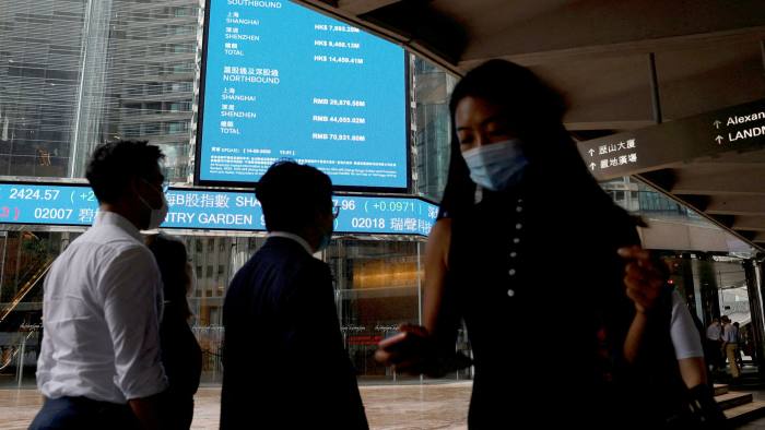 People wearing protective masks walk past screens outside the Hong Kong Exchanges