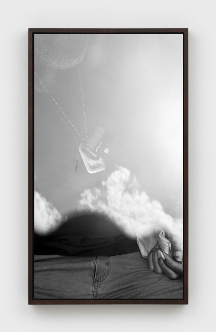 Black and white photo of a man sitting down, but it’s hard to see him for the reflection of the sky