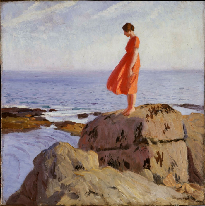 A woman in a red dress stands on a rock by the sea, looking down at the water