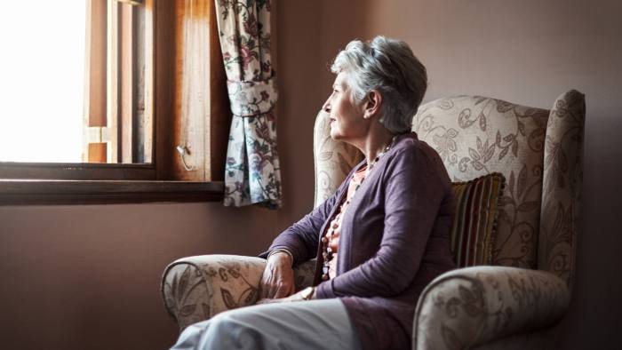 senior woman sitting alone in her living room looking out a window