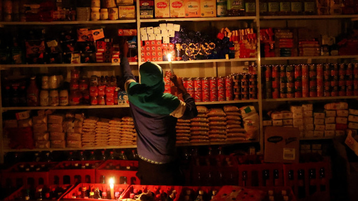 A shop owner picks an item for a customer by candlelight during power outages by South African utility Eskom
