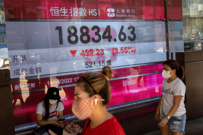 People walk past an electronic billboard showing the Hang Seng Index