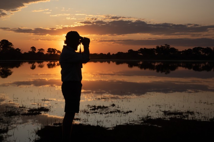 Wilderness guide Alan McSmith bird-watching at sunset, near camp Kwapa in the Okavango Delta