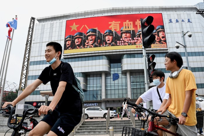 Three young men cycle past an advert for the Chinese People’s Liberation Army