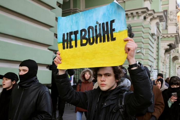 A male protester carries a placard painted in the blue and yellow of the Ukrainian flag and with the words ‘No to war’ in Russian