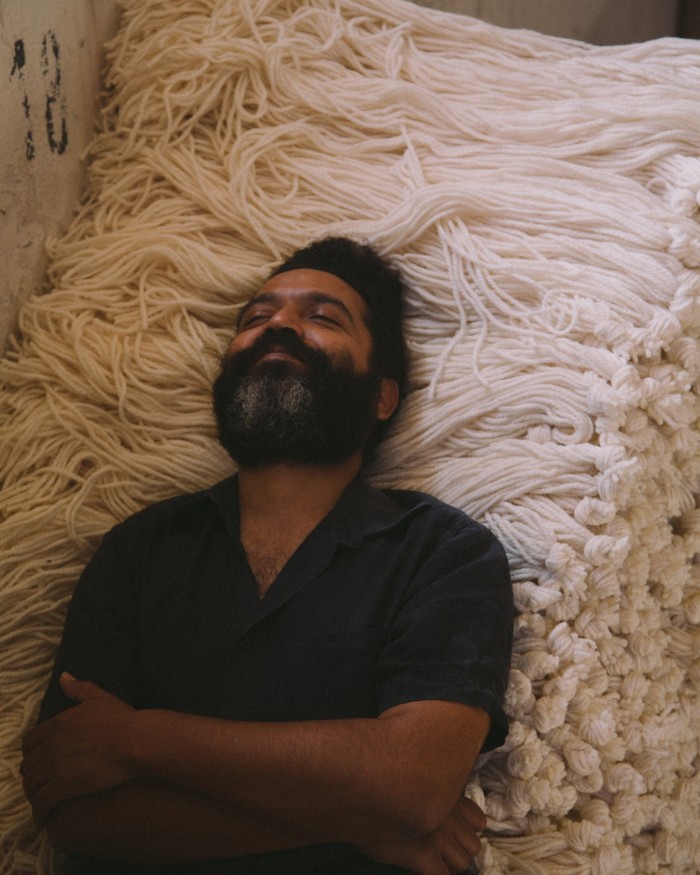 Close-up of a bearded man lying on a pile of white natural raw wool, smiling 