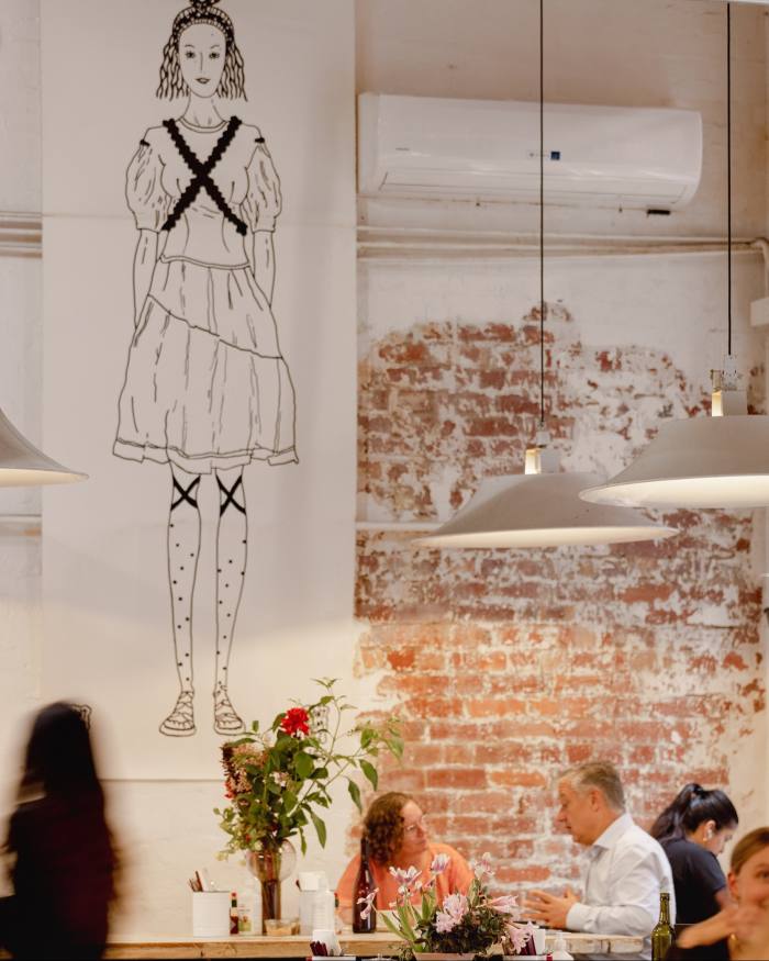 A 10-foot-tall cartoon of a woman hanging in front of a bare-brick wall behind customers at tables at Manchester Press