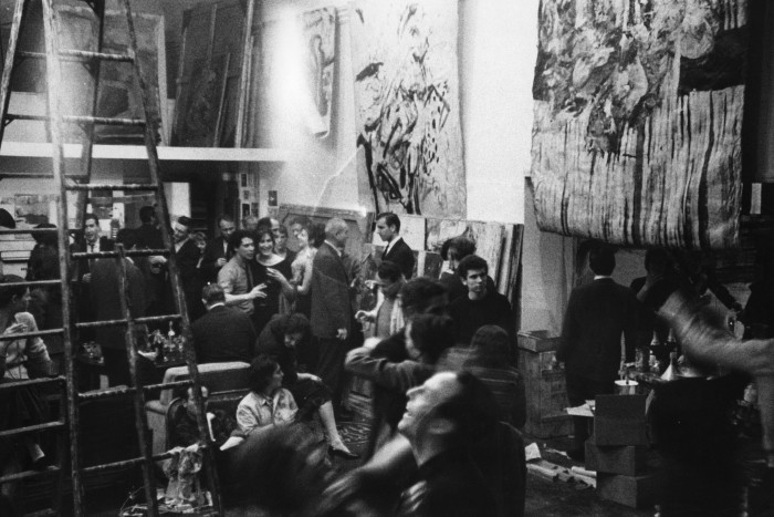People mingle at a party in a loft artist’s studio with paintings on the walls