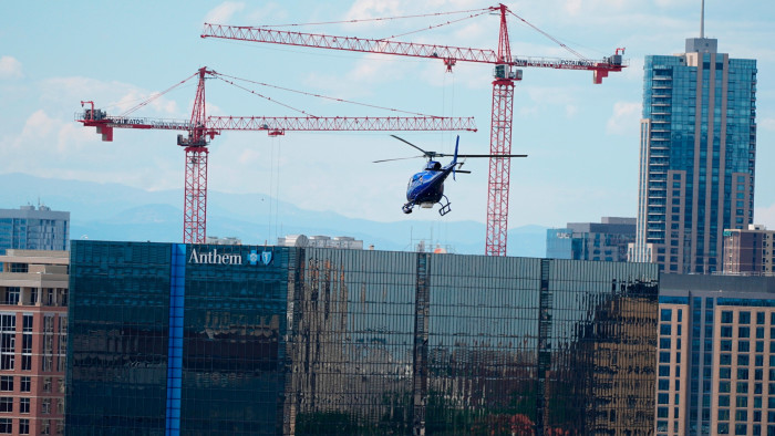 Helicopter flies above a building with construction cranes in background