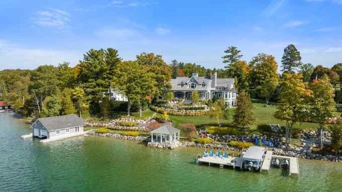 A luxurious lakefront property with a boathouse and surrounded by lush trees and verdant grass