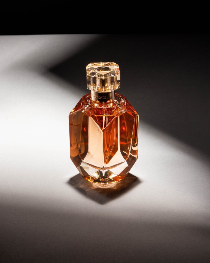 A transparent geometric perfume bottle with amber-colored liquid inside, topped with a faceted clear cap