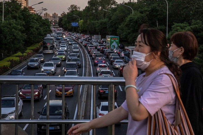 Women wearing face masks cross over a road jammed with cars during rush hour in Beijing. Indications from China are of a sharp rise in individual car use