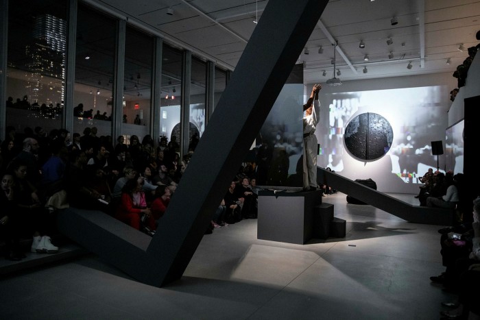 A woman performs in a dark geometric space