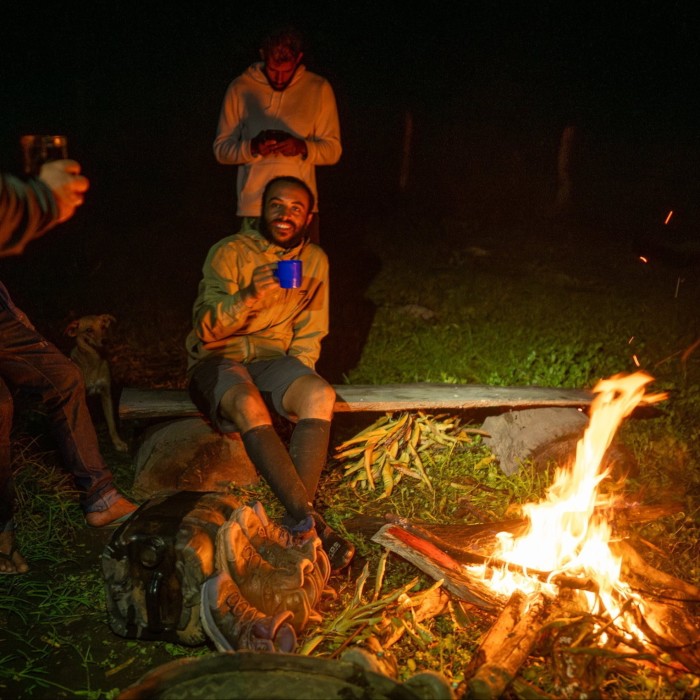 Men sit drinking around a camp fire in the dark 