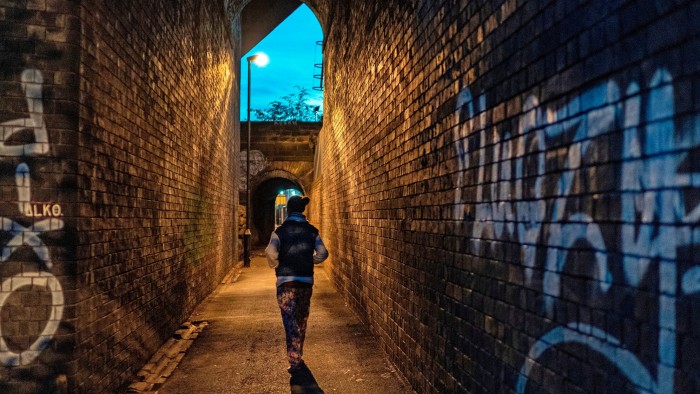 A woman walking alone down a dimly lit alley with graffiti 