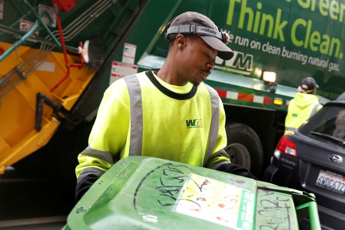 An employee of Waste Management collecting a bin on the street in Oakland, California 