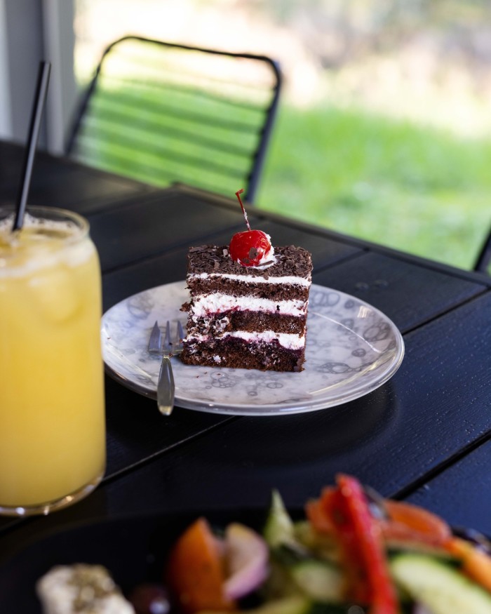 A chocolate and cream gateau with a glass of cherry on top of it, beside a glass of orange-coloured fruit juice at Melissa, an eatery on the Ruffey Creek Trail