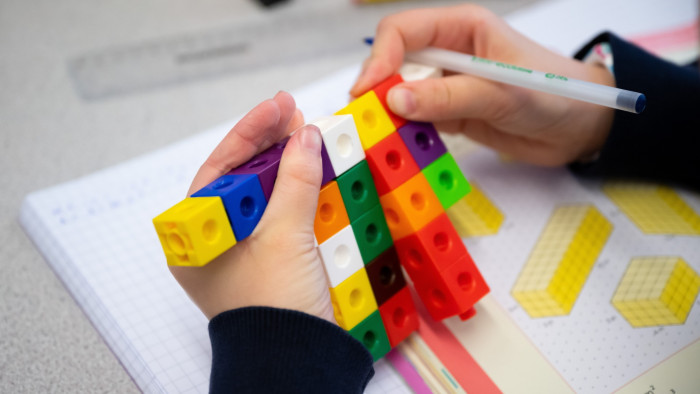 View of a primary school child’s hands  using coloured cubes to study maths in a school 