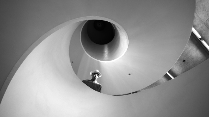 Black and white film still of a man looking over a curving concrete staircase