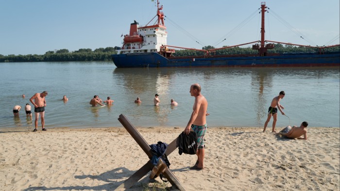People sit on a public beach and swim in the Danube as boats pass by on the water on August 20 2023 in Izmail, Ukraine