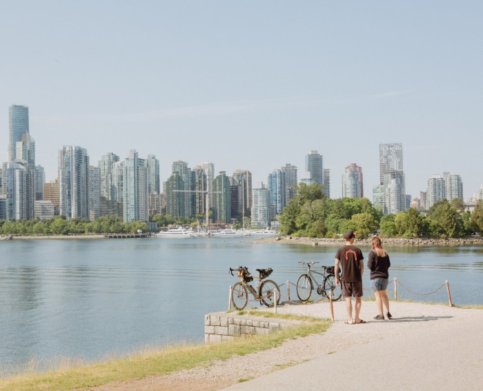 A male and female cyclist have dismounted at the start of the Stanley Park Seawall route to look across the water to downtown Vancouver and the city’s marina  