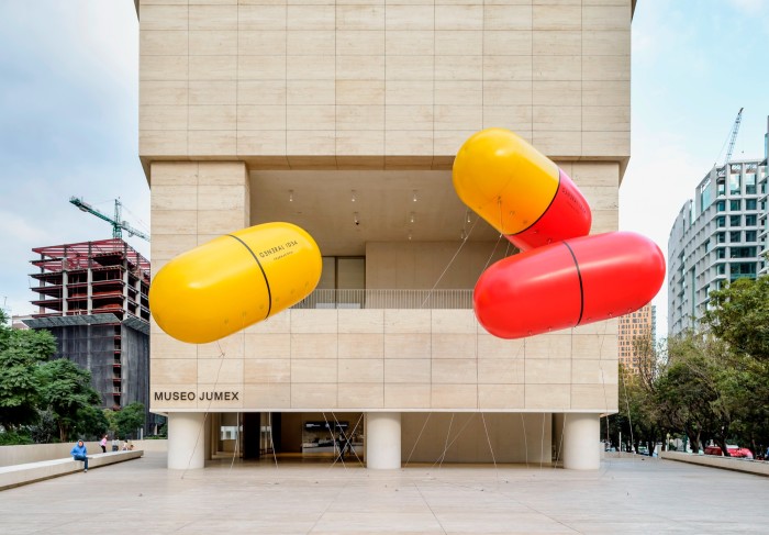 Very large inflated capsule pills in red and yellow hanging outside a pale museum